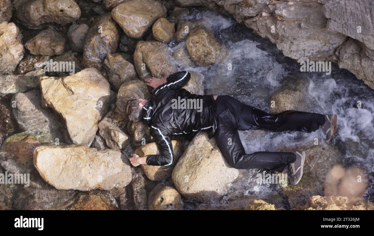 Corpse of man on shore. Stock. Body of man on rocks with waves on shore. Bandit is lying unconscious on shore Stock Photo