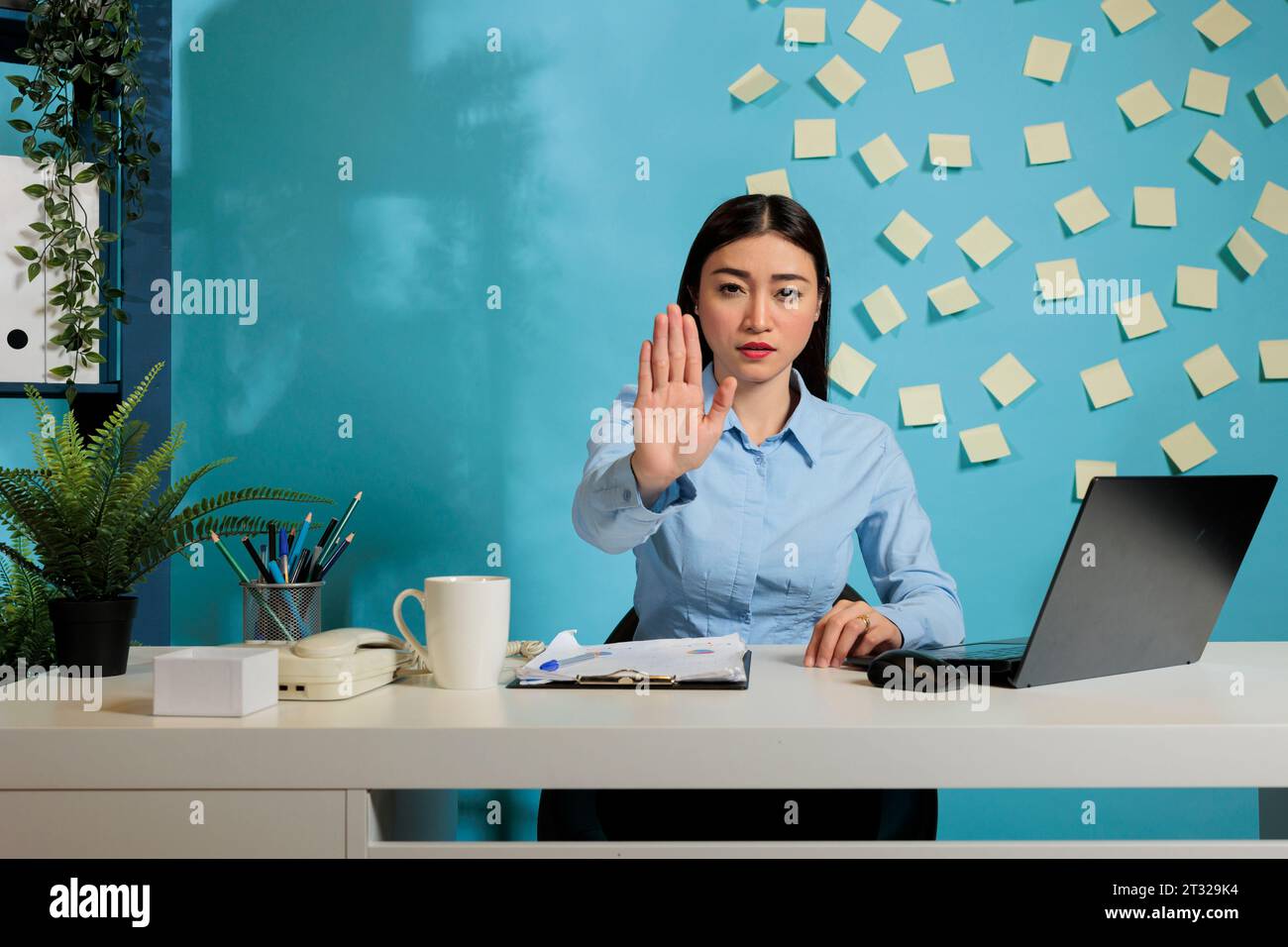 Woman seated at office desk showing rejection with the palm of her hand