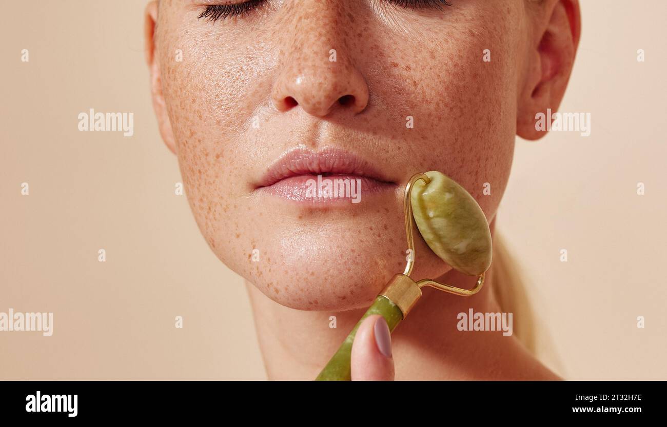 Close-up high detailed cropped shot of a young using a roller on her freckled skin Stock Photo