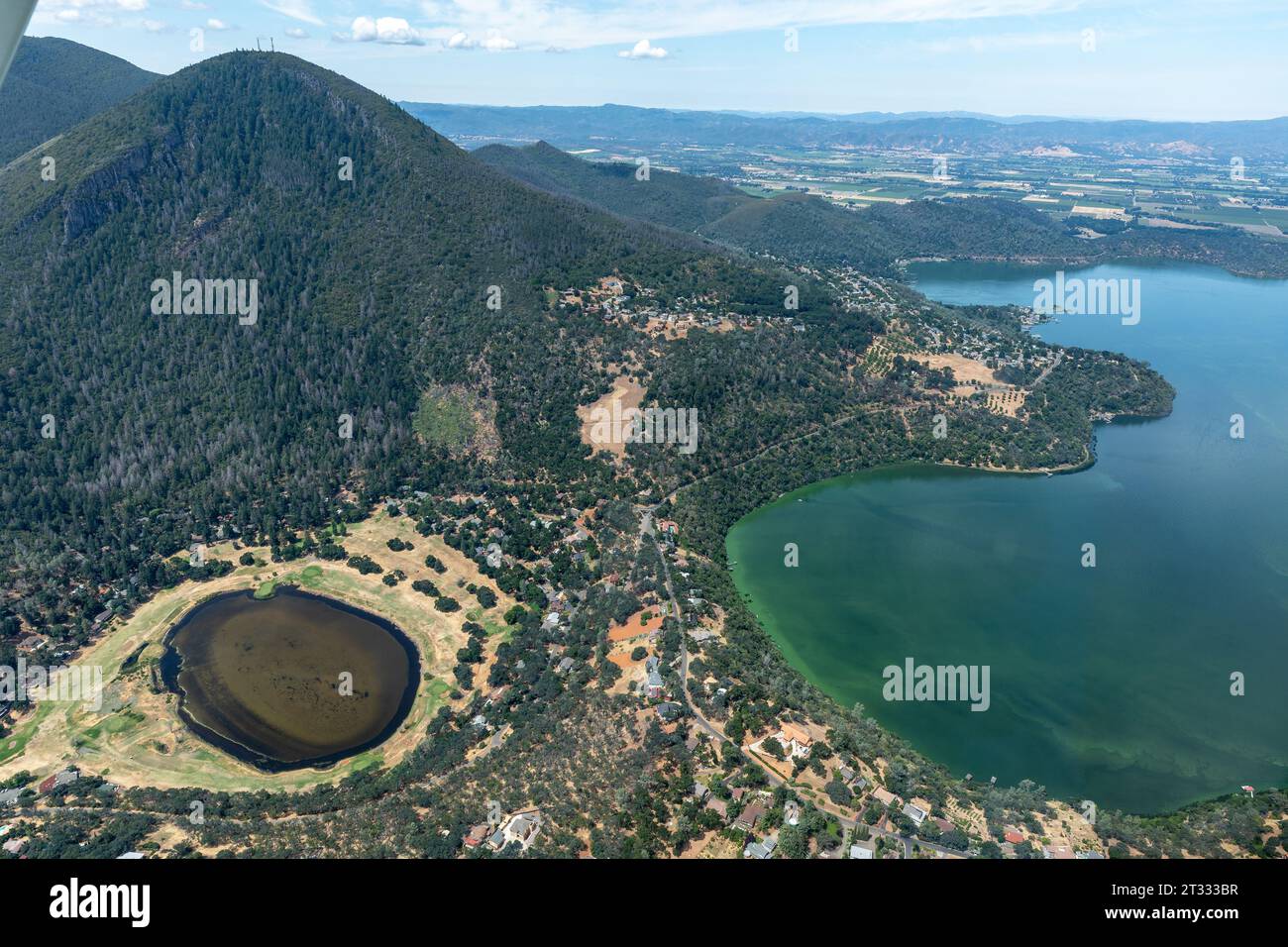 Topography of clear lake area with Green mountainsides farm lands and rolling hills which run off and form blooms of green algae in the lake Stock Photo