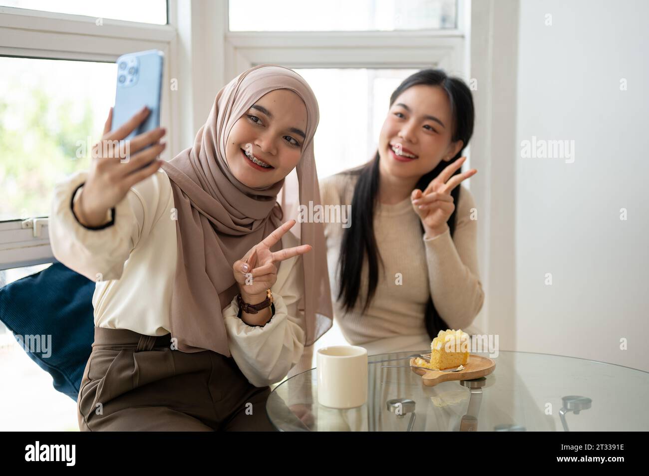 A beautiful and happy young Asian-Muslim woman is taking selfies with her friend while enjoying in a cafe. Stock Photo