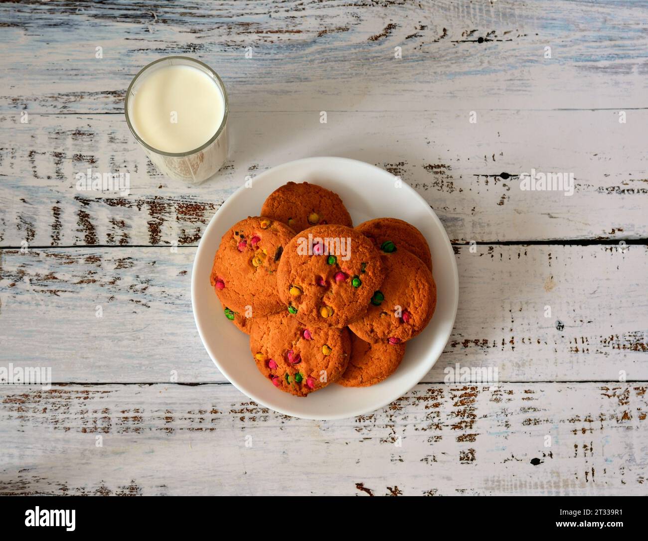 A white plate with several fresh oatmeal cookies and a glass of hot milk on a light wooden table. Top view, flat lay. Stock Photo