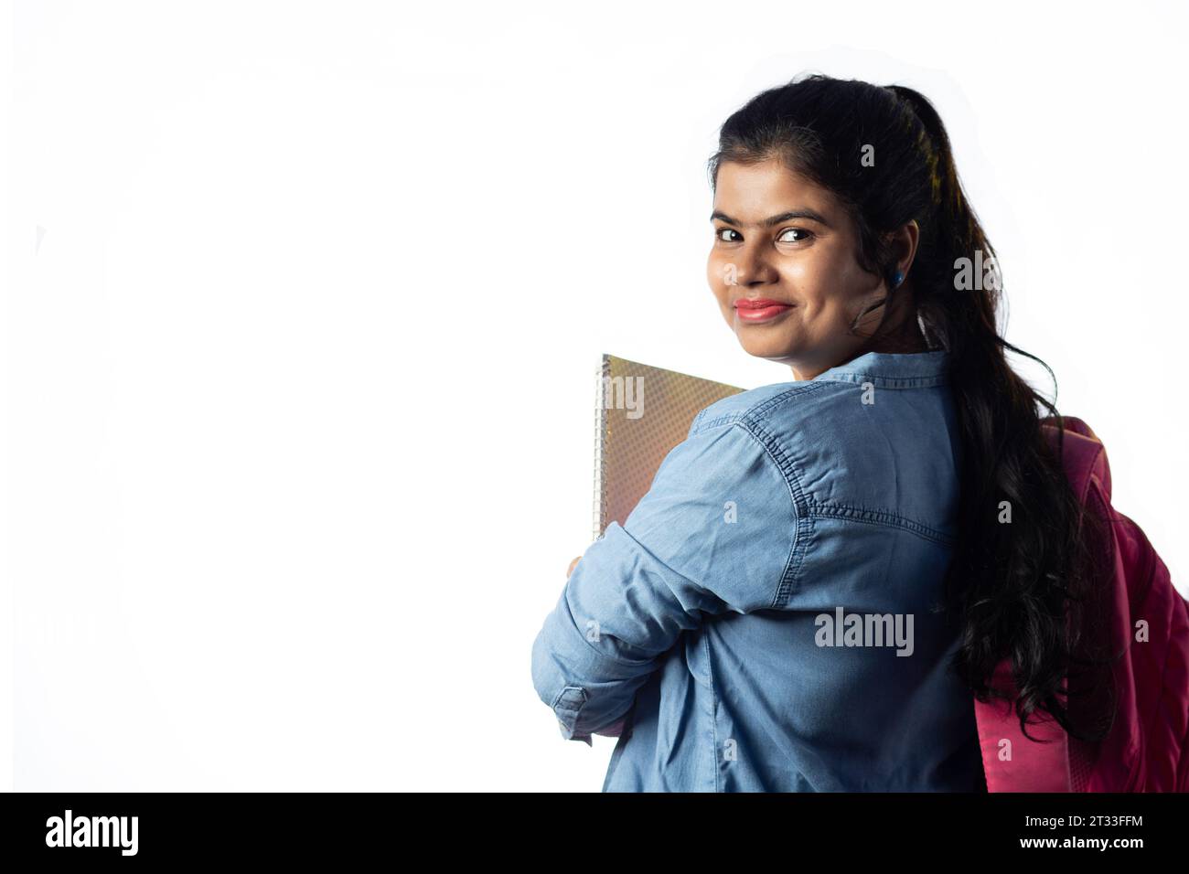 A pretty young Indian girl with books in hand and backpack standing ...