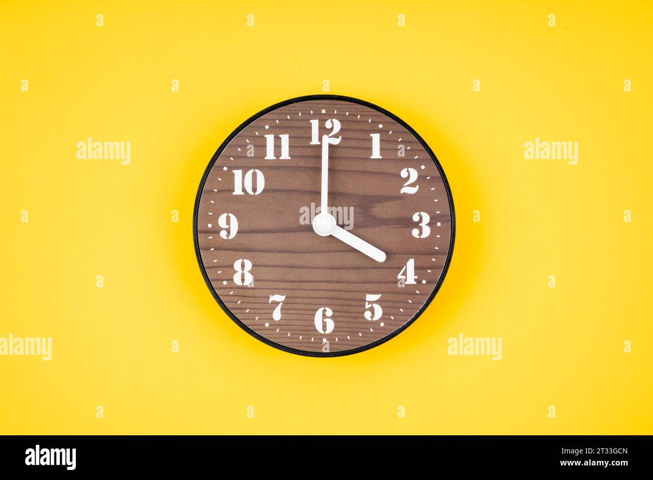 Retro wooden clock at 4 O' clock on yellow color background Stock Photo