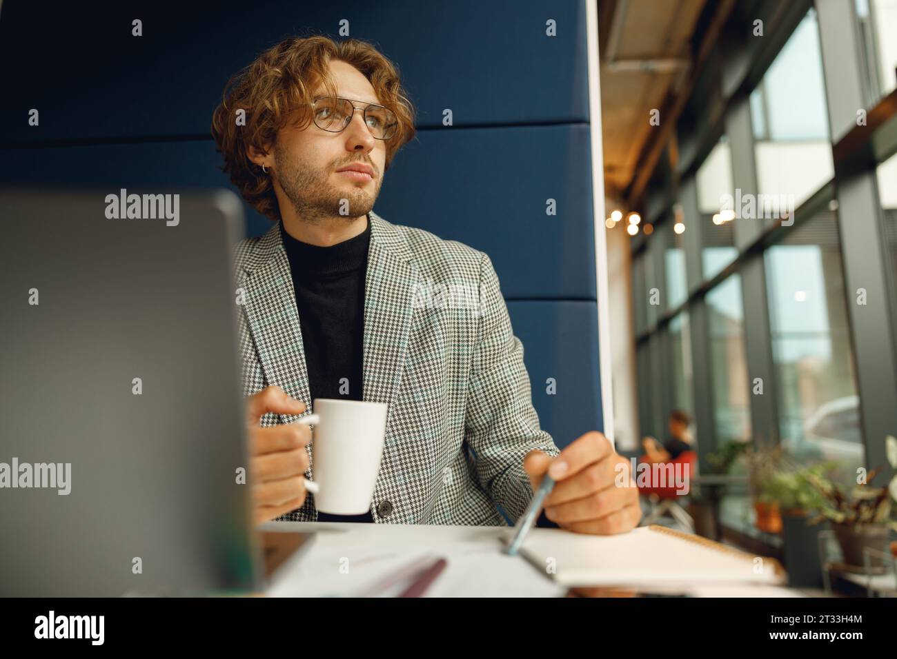 Focused businessman working on project while using laptop and making notes while sittting in office Stock Photo