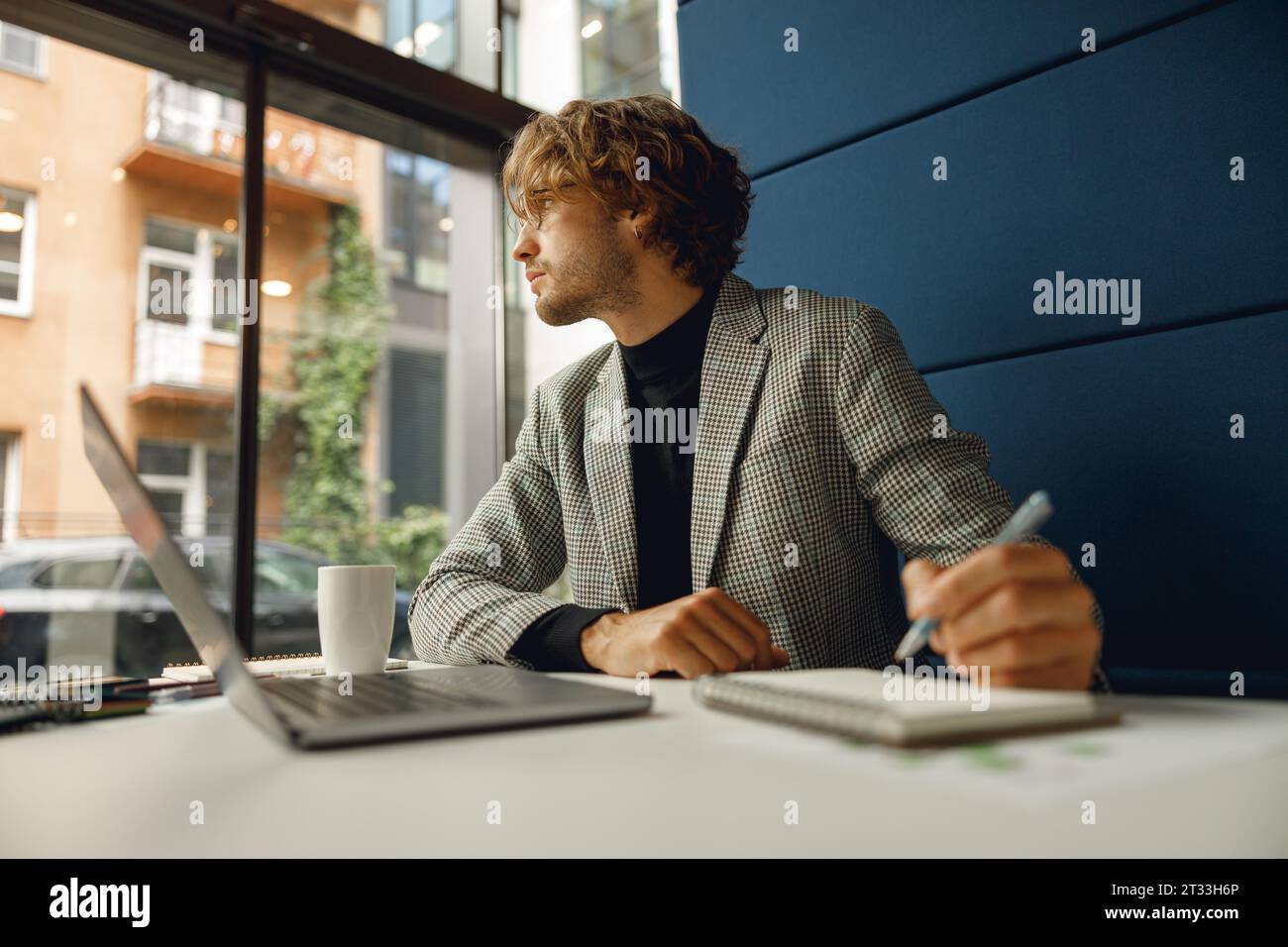 Handsome businessman working on project while using laptop and making notes while sittting in office Stock Photo