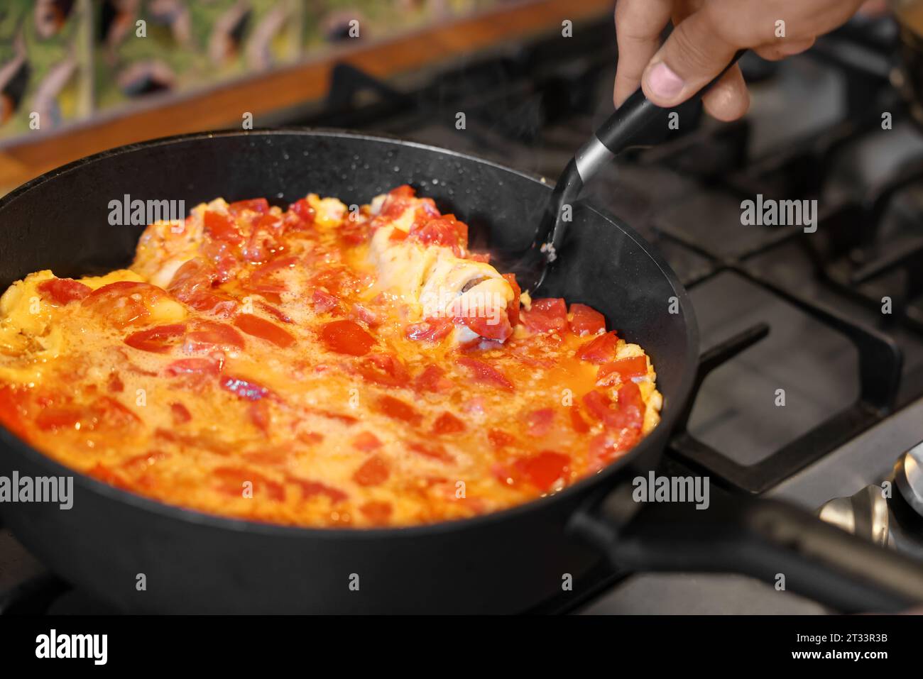 Man cooking tasty fried eggs with tomatoes on stove, closeup Stock