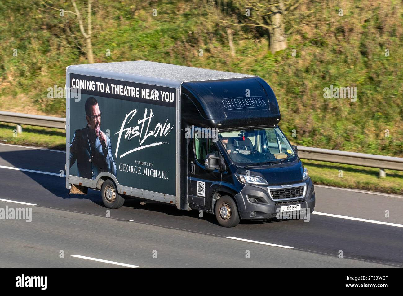 'Fast Love' A tribute to George Michael Entertainment advertising on 2-10 Peugeot Boxer 335 Pro L3h2 Blue Hdi Bluehdi 130 L3H2 LWB LCV Medium Roof Panel Van Diesel 1997 cc; travelling at speed on the M6 motorway in Greater Manchester, UK Stock Photo