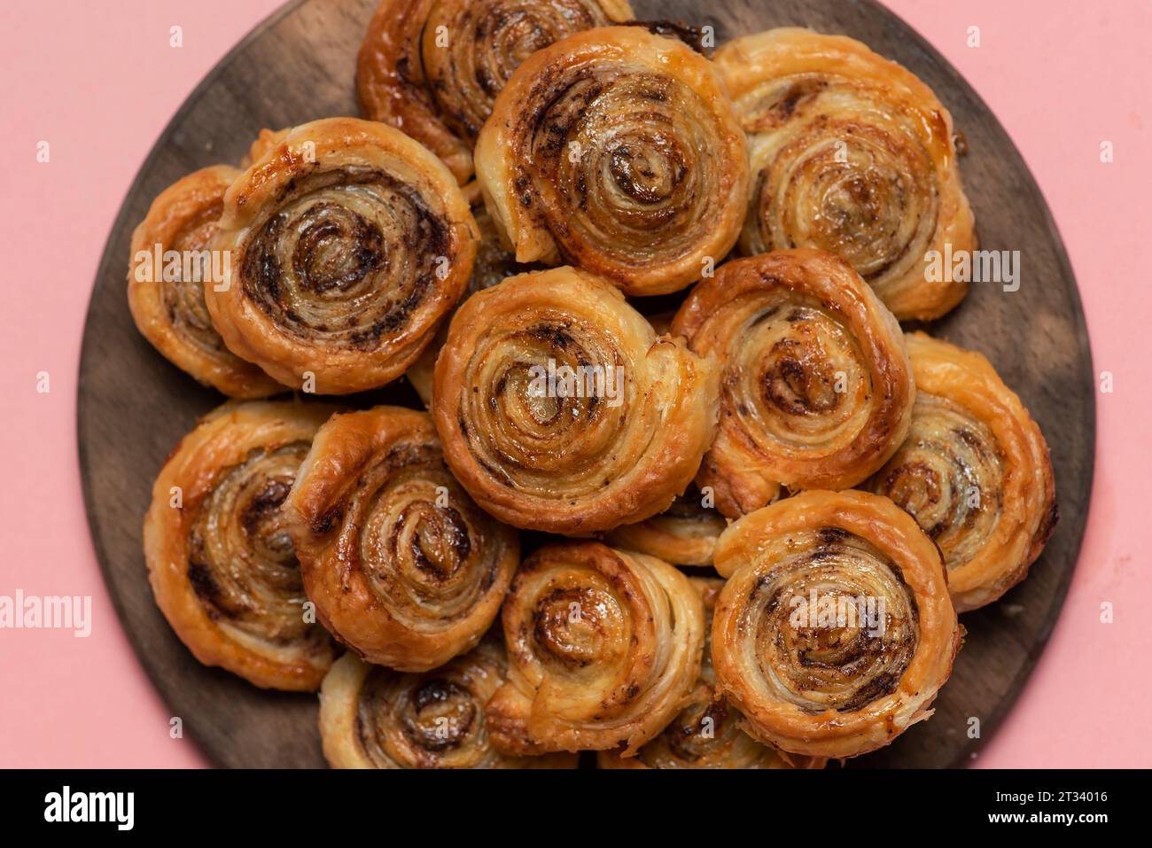 Freshly baked sweet and crispy cinnamon rolls. On a wooden plate and pink background Stock Photo