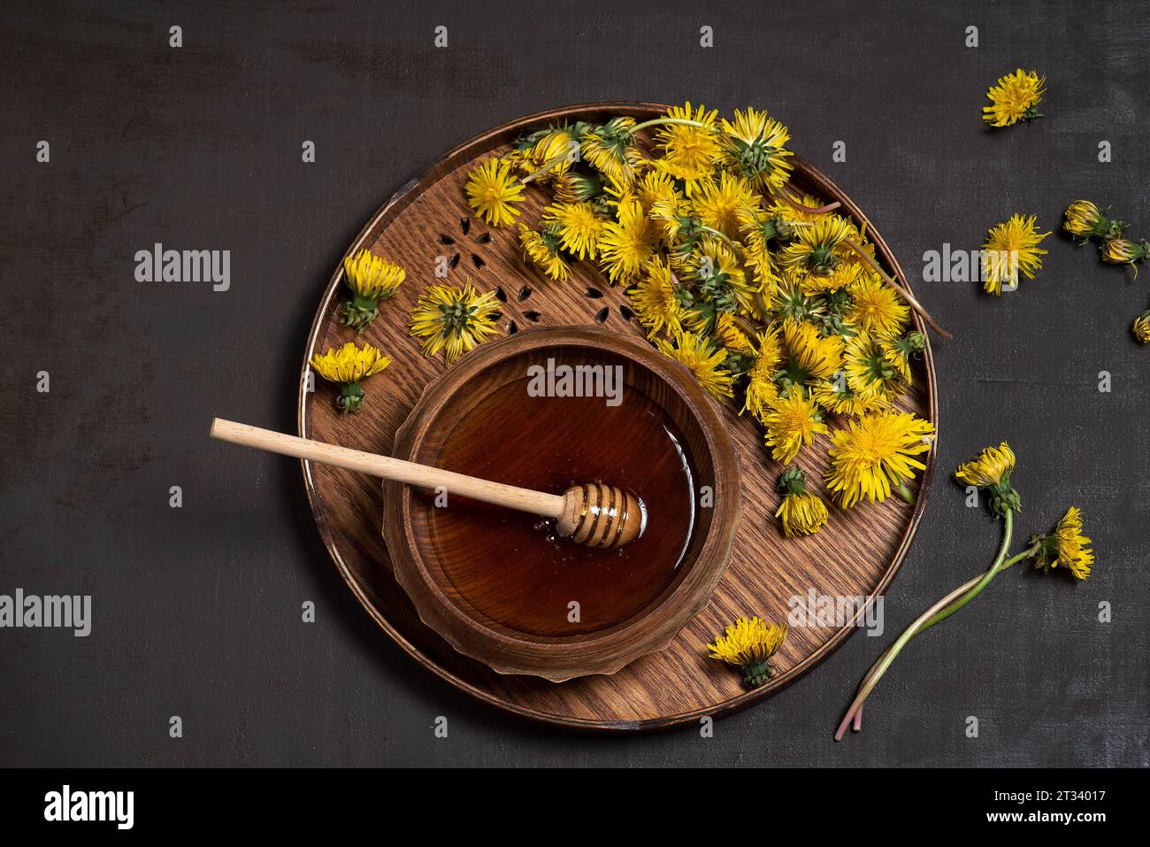 Dandelion honey with dandelion leaves and flowers in a wooden bowl on a black background. Top view Stock Photo