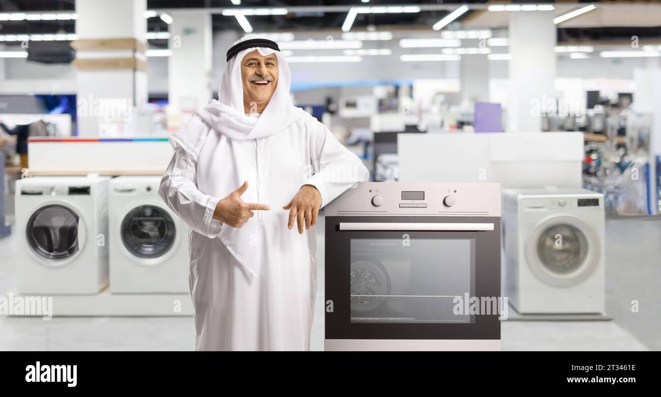 Mature arab man standing in a shop with washing machines and leaning on an oven Stock Photo