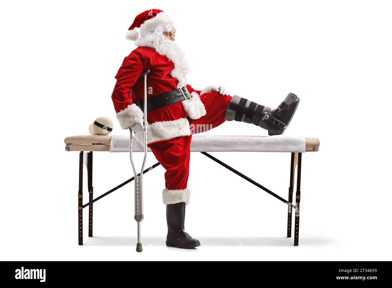 Profile shot of Santa claus with a foot brace and crutch sitting on a medical bed isolated on white background Stock Photo