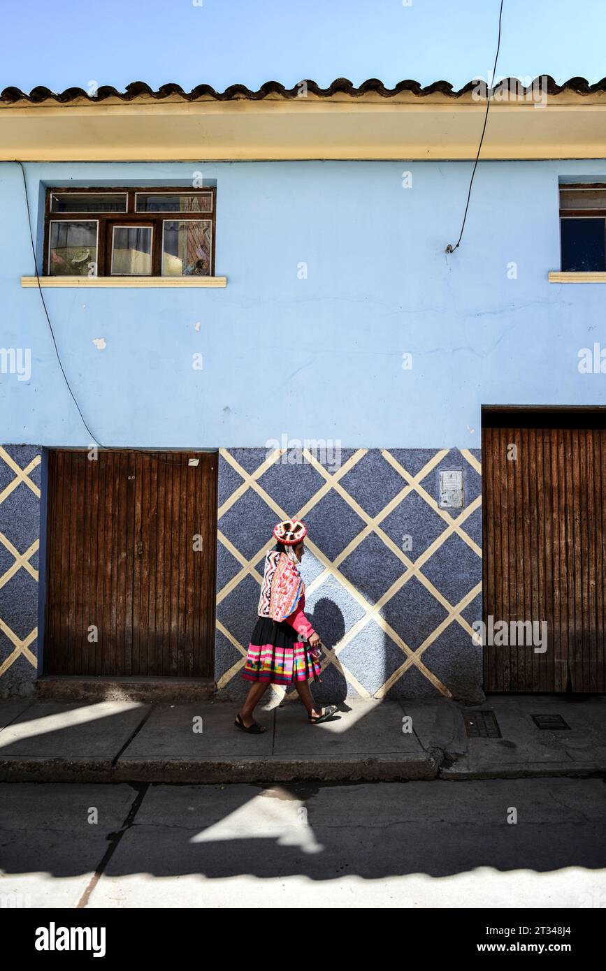 A young Quechuan woman walks into a lone sunny spot on a shady street in Urubamba. Stock Photo