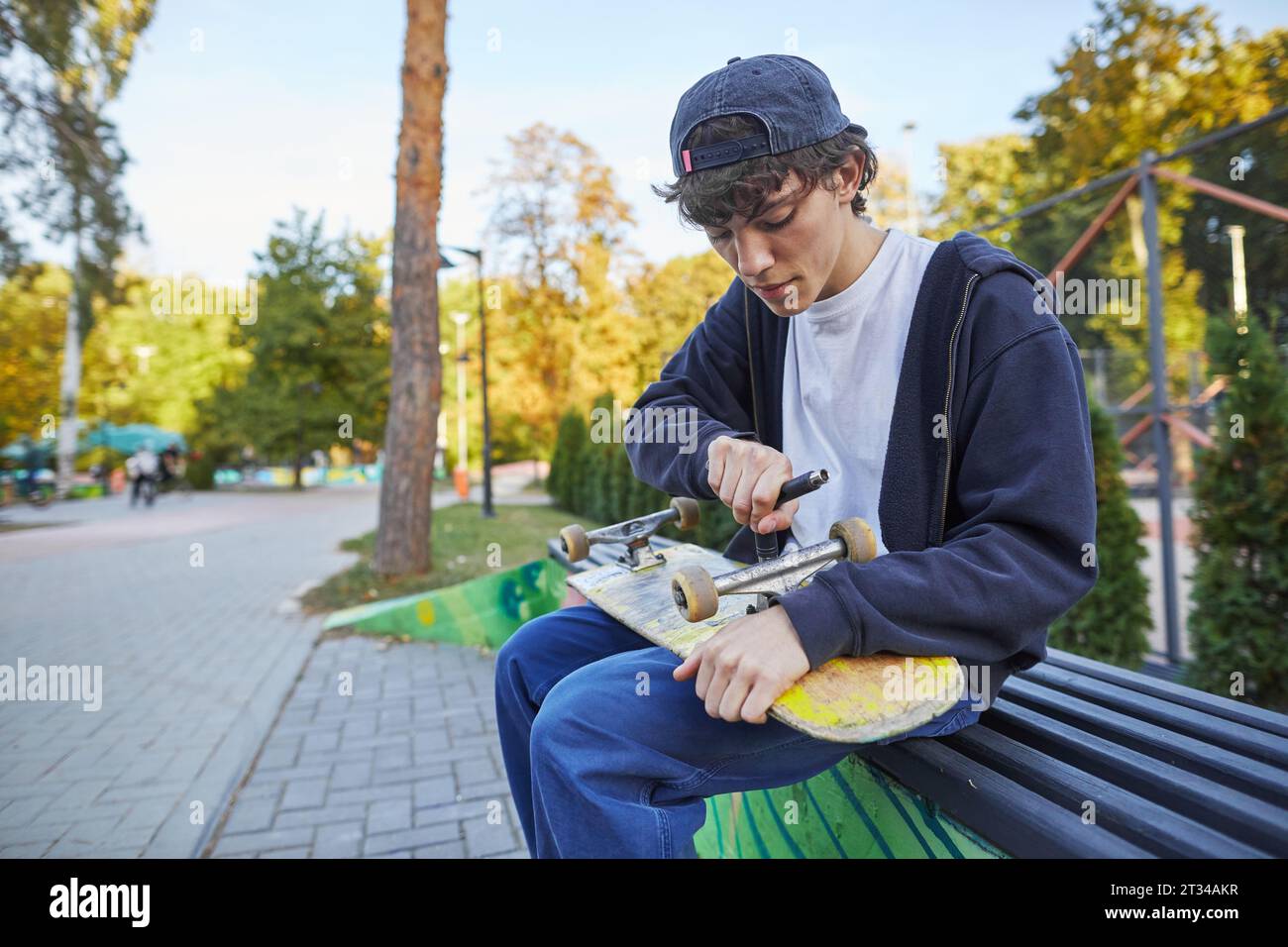 skateboarder repairing his skate in the park on a bench Stock Photo