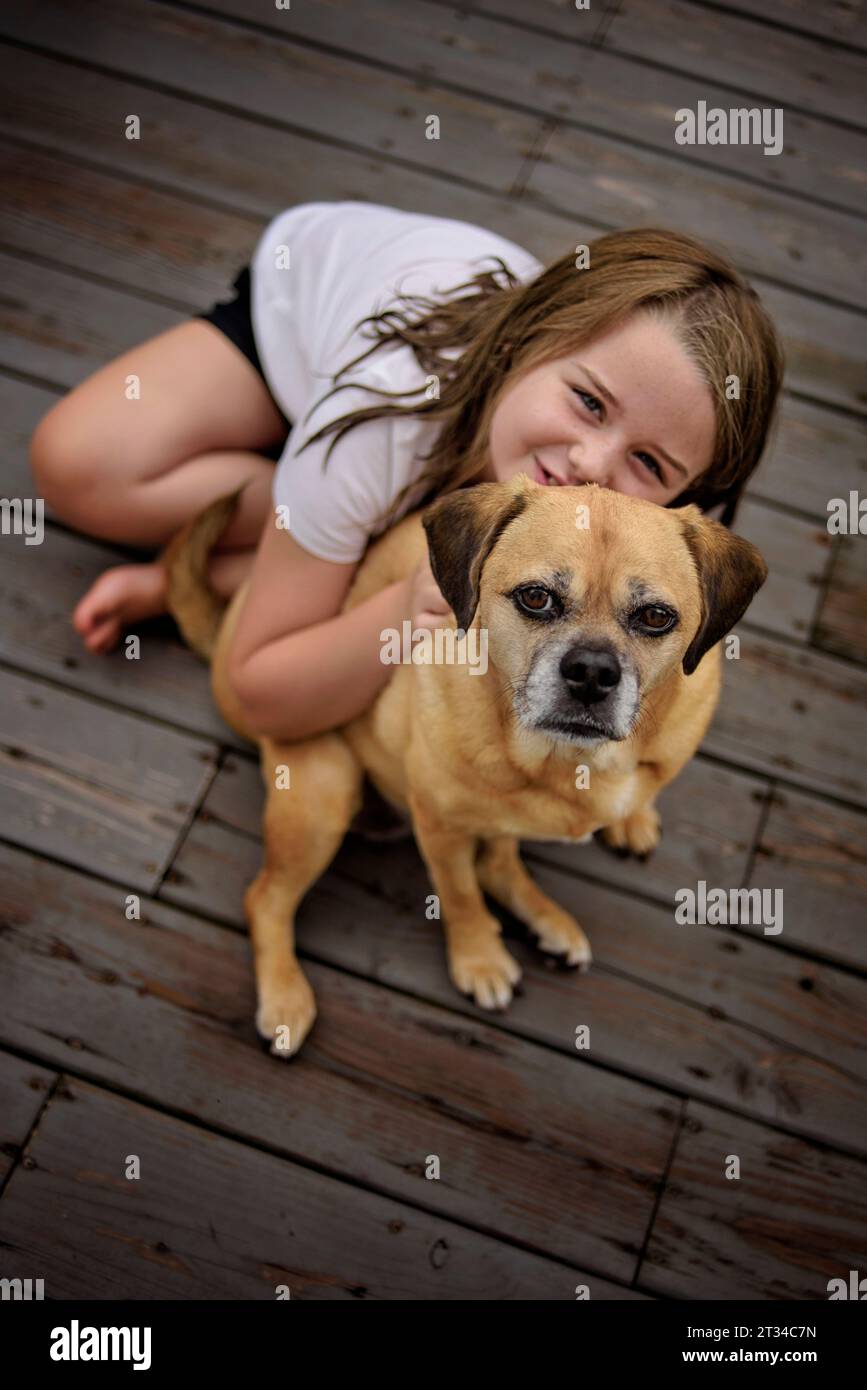 Happy little girl petting brown Puggle dog outside Stock Photo