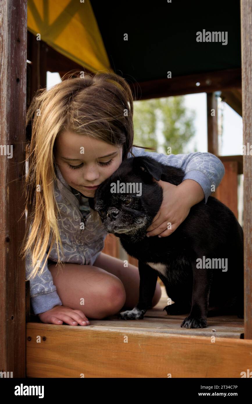 Little girl hugging black pug dog in playhouse Stock Photo
