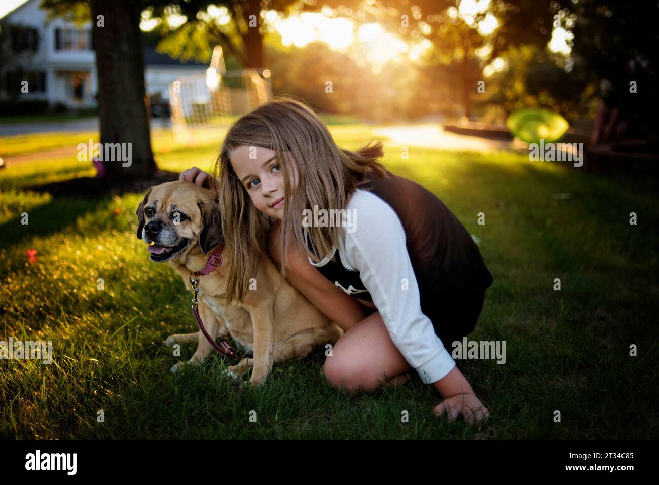 Young girl sitting with smiling and panting puggle dog in back yard Stock Photo