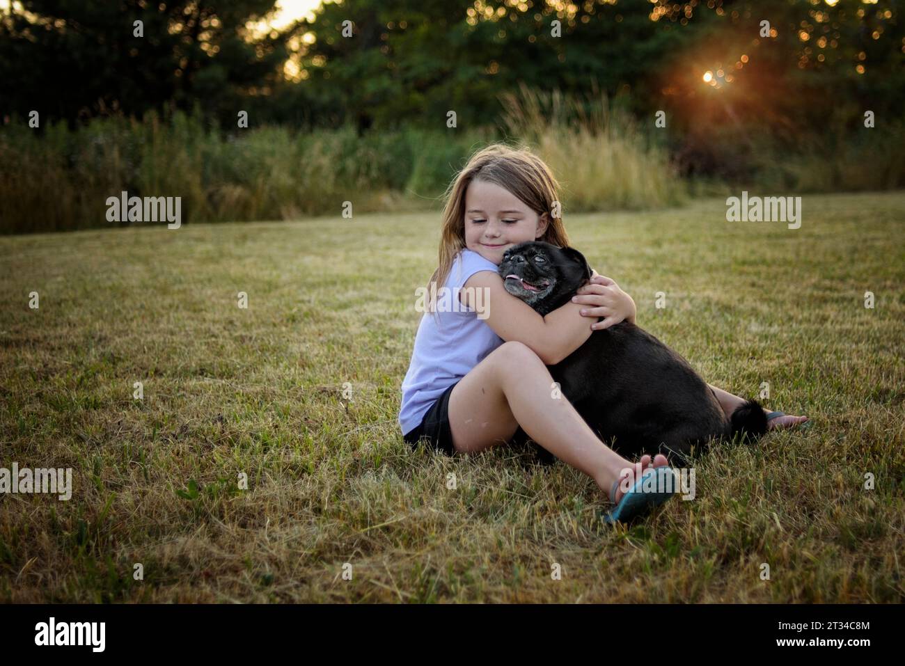 Little girl hugging black pug puppy outside Stock Photo