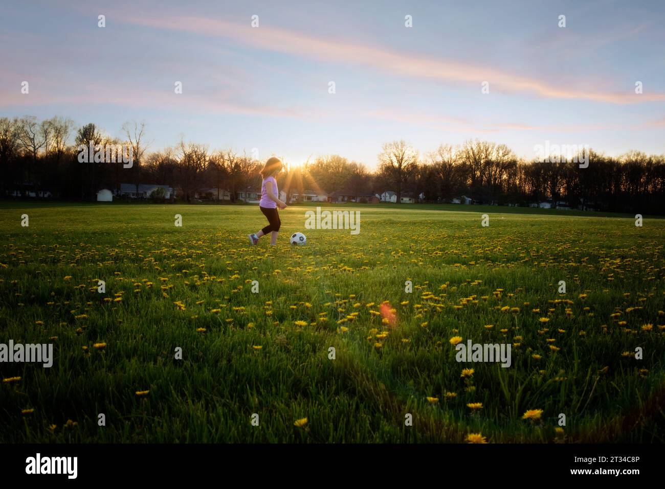 Young girl kicking soccer ball through field in spring Stock Photo
