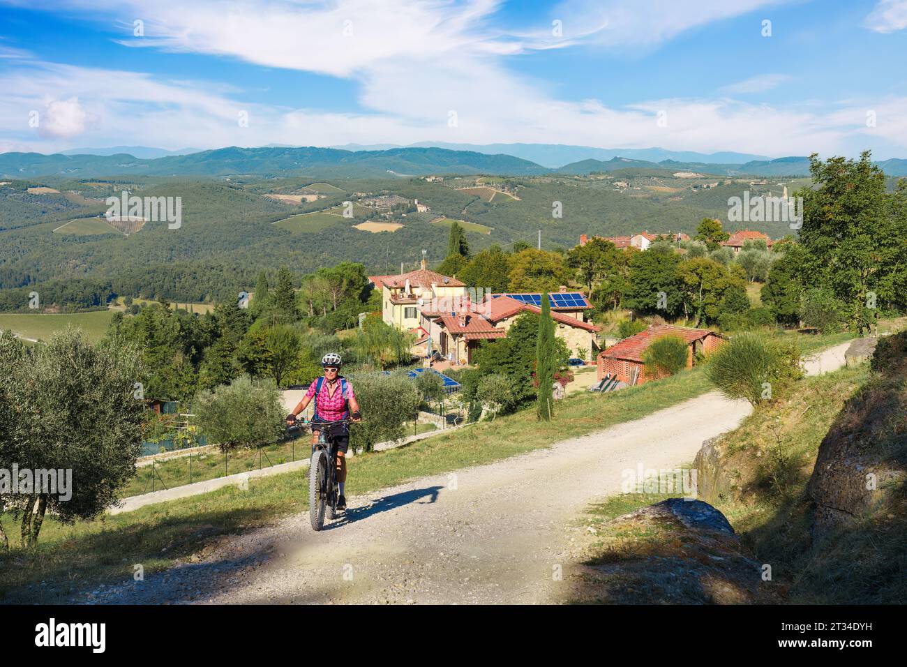nice senior woman riding her electric mountain bike between cypress and olive trees in the Ghianti Area of Tuscany,Italy Stock Photo