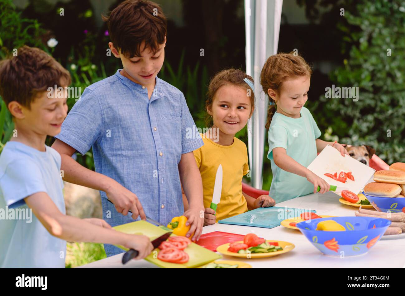 Happy children cooking together hot dogs and vegetables for holiday outdoor party Stock Photo