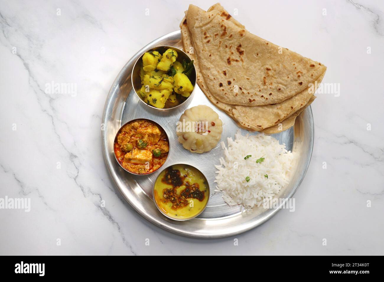 Indian vegetarian Thali or platter includes Aloo ki sabji, dal rice, Roti bhaji, Matar Paneer, Sheera or suji ka halwa, chapati. Indian food, sheera. Stock Photo