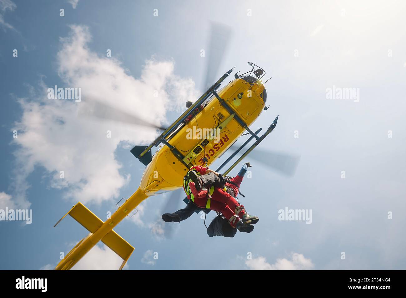 Two paramedics hanging on rope under flying helicopter emergency medical service. Themes rescue, help and heroes. Stock Photo