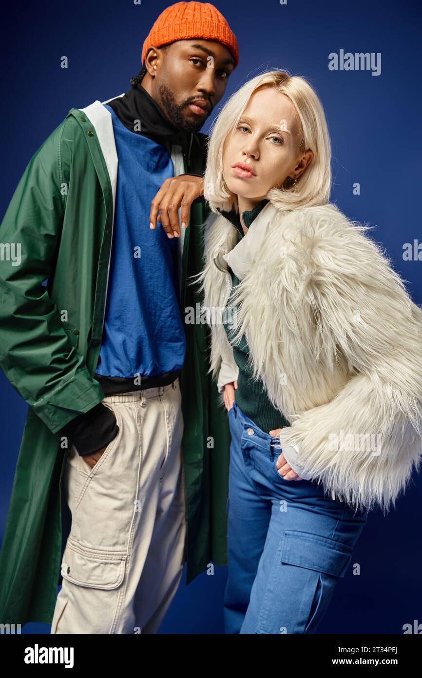 multicultural couple posing with hands in pockets, woman in faux fur jacket and african american man Stock Photo