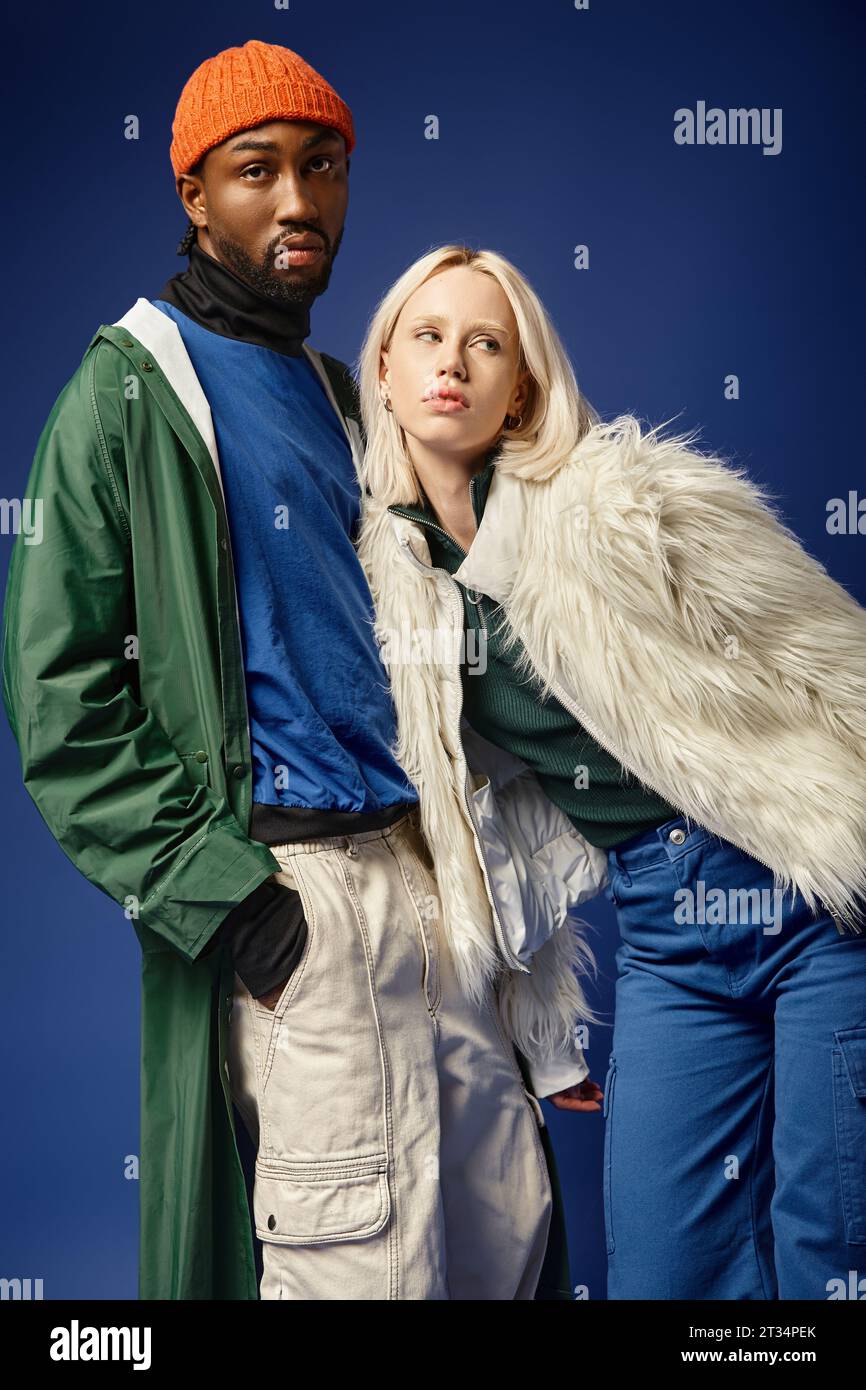 interracial couple posing on blue backdrop, woman in faux fur jacket and african american man Stock Photo