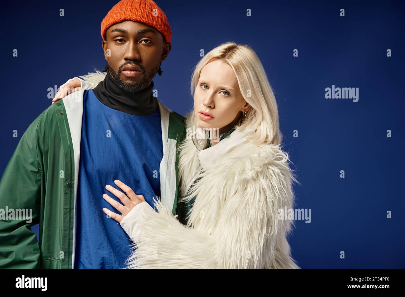 young woman embracing african american man in winter attire of blue backdrop, multiethnic couple Stock Photo