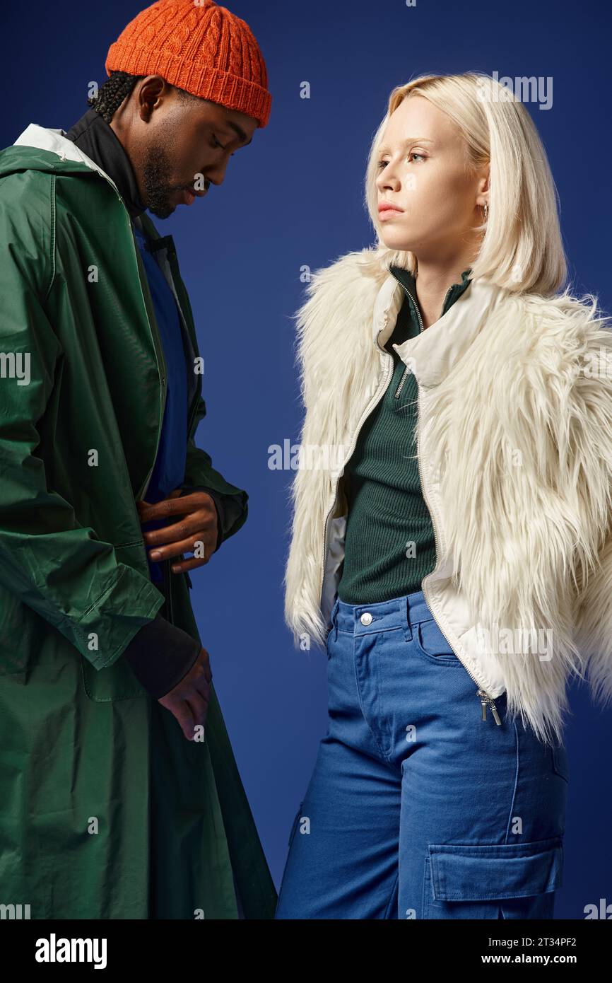 blonde woman posing with african american man in winter attire of blue backdrop, diverse models Stock Photo
