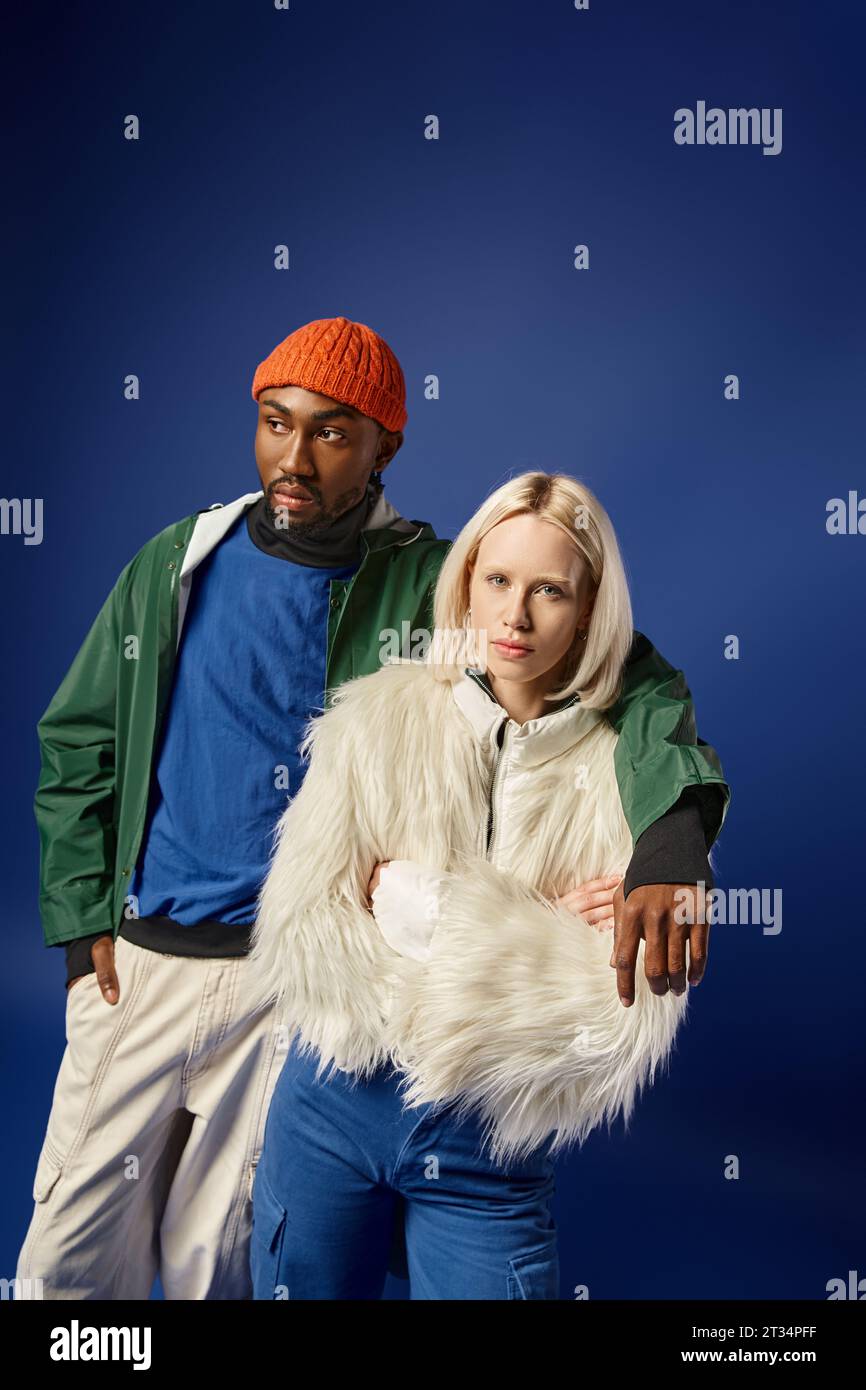 african american man hugging young woman in winter attire, diverse couple on blue backdrop Stock Photo