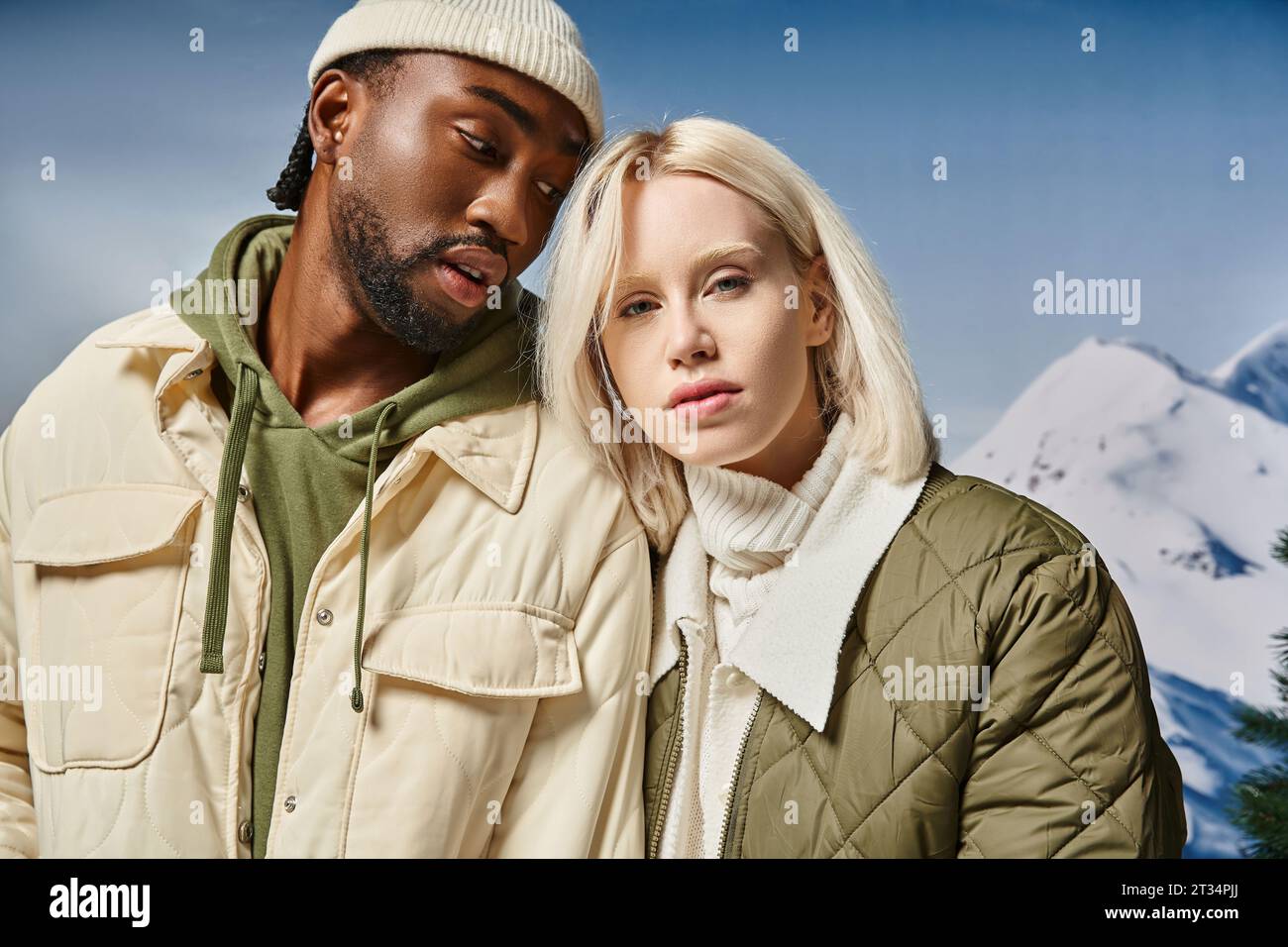 attractive couple in stylish modern outfits with snowy mountain on backdrop, winter concept Stock Photo