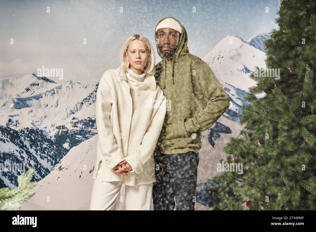 beautiful stylish couple posing together under snowfall in trendy warm jackets, winter concept Stock Photo