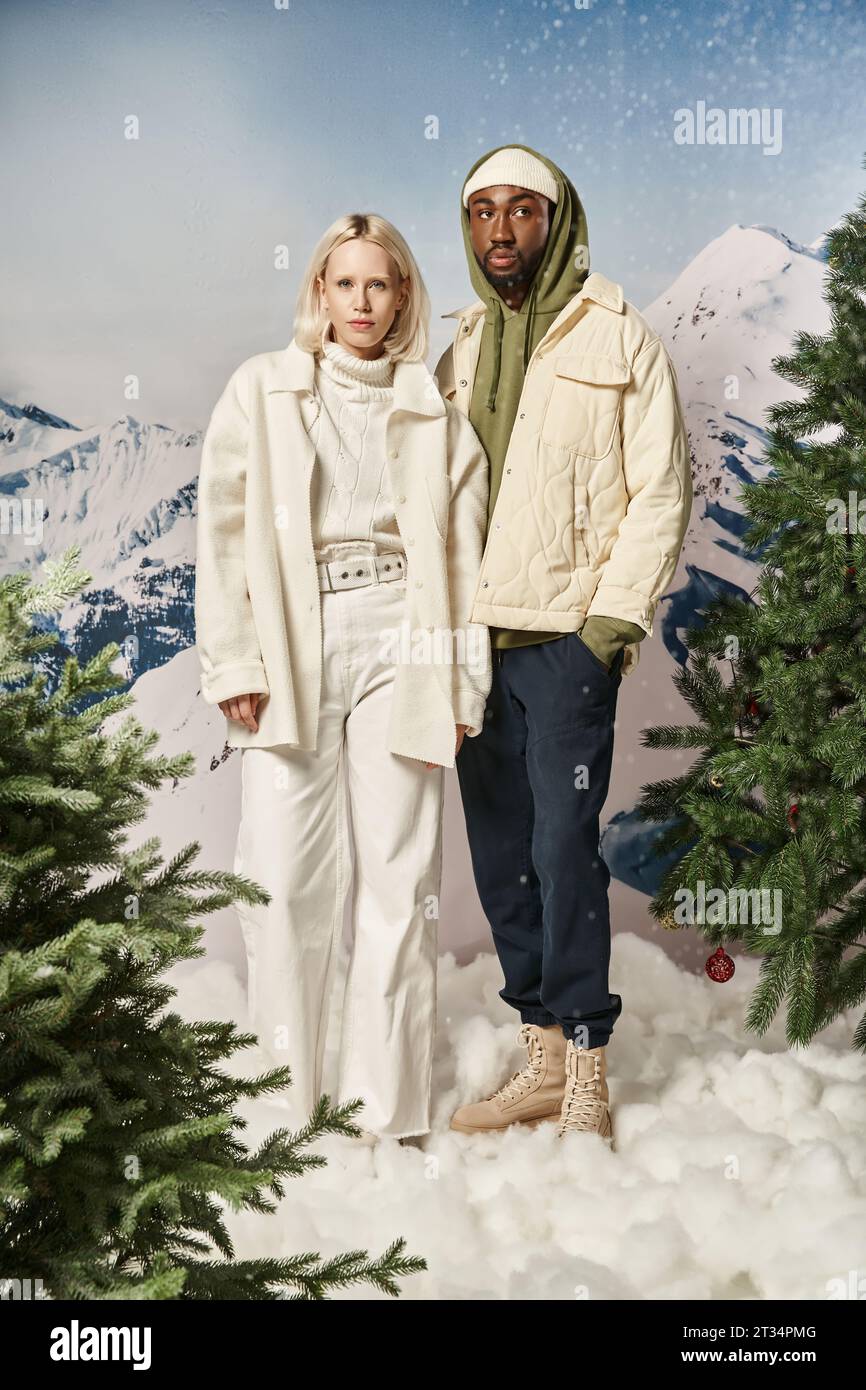attractive diverse couple posing together in winter warm attire with snowy backdrop, fashion concept Stock Photo