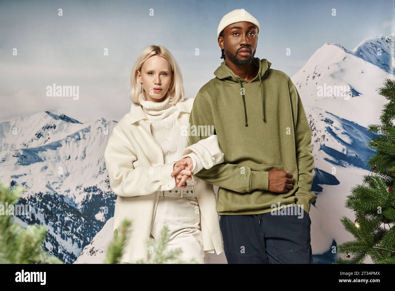 stylish blonde woman standing with african american boyfriend with mountain backdrop, winter fashion Stock Photo