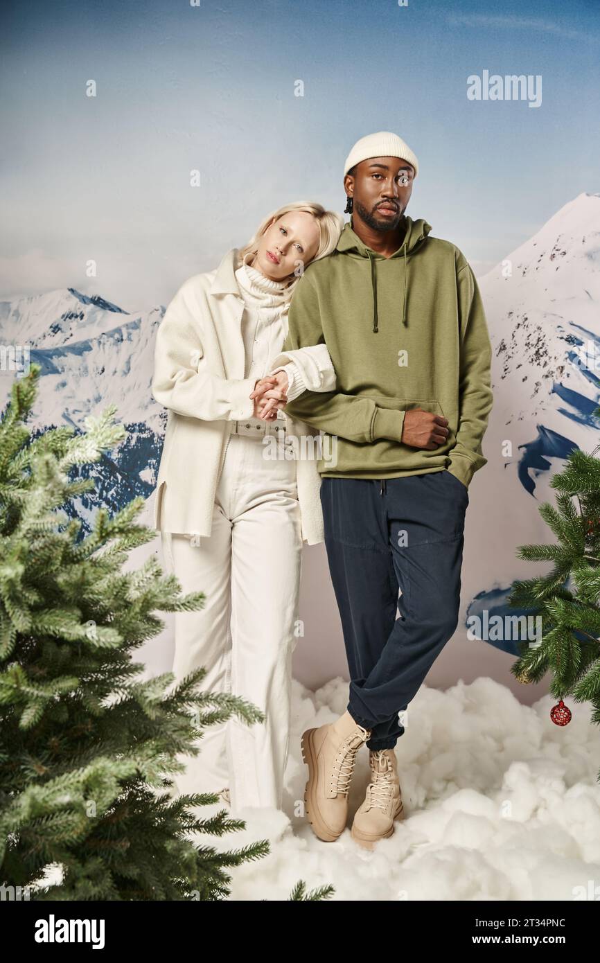 full length of stylish interracial couple in winter attire standing together with mountain backdrop Stock Photo