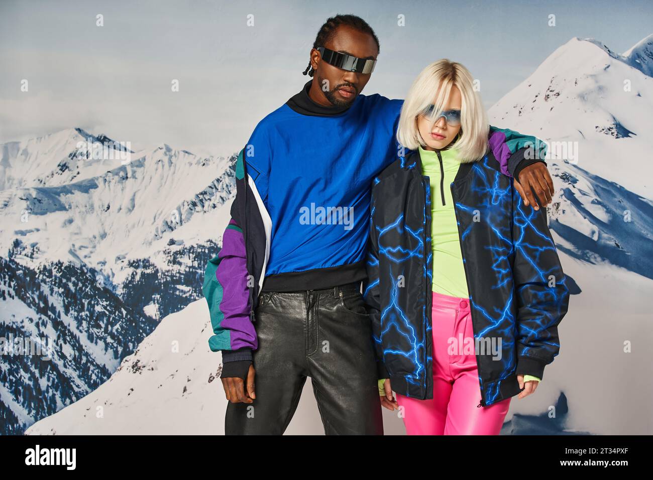 young interracial couple hugging and looking at camera with mountain backdrop, winter concept Stock Photo