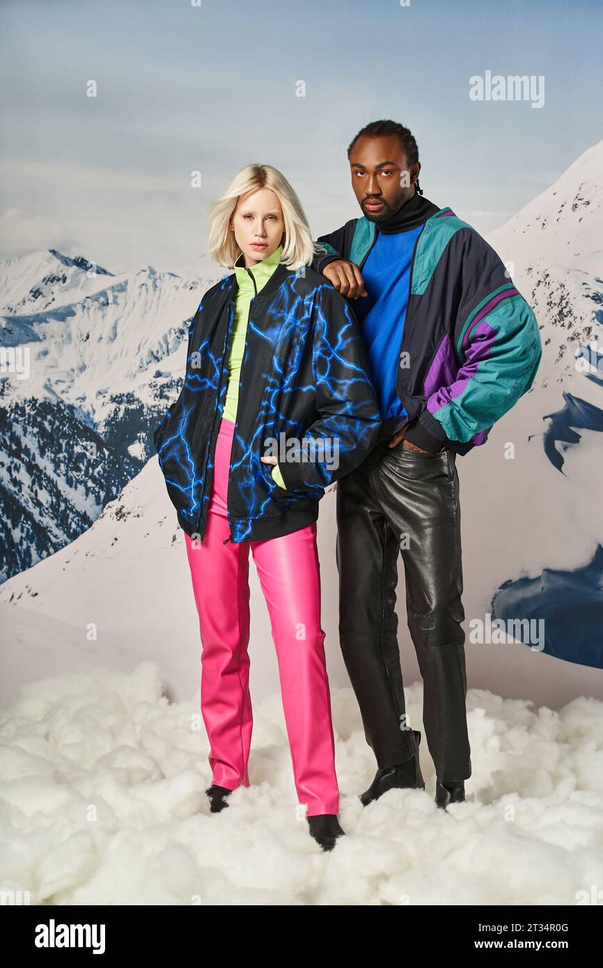 stylish young couple in warm attire posing with hand on shoulder with snowy backdrop, winter concept Stock Photo