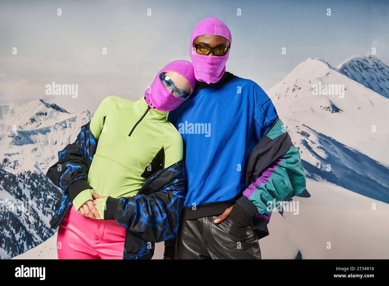 stylish diverse couple in pink balaclavas and sunglasses hugging and posing together, winter concept Stock Photo