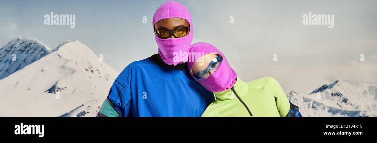 young multiethnic couple in pink balaclavas and sunglasses hugging, winter concept, banner Stock Photo