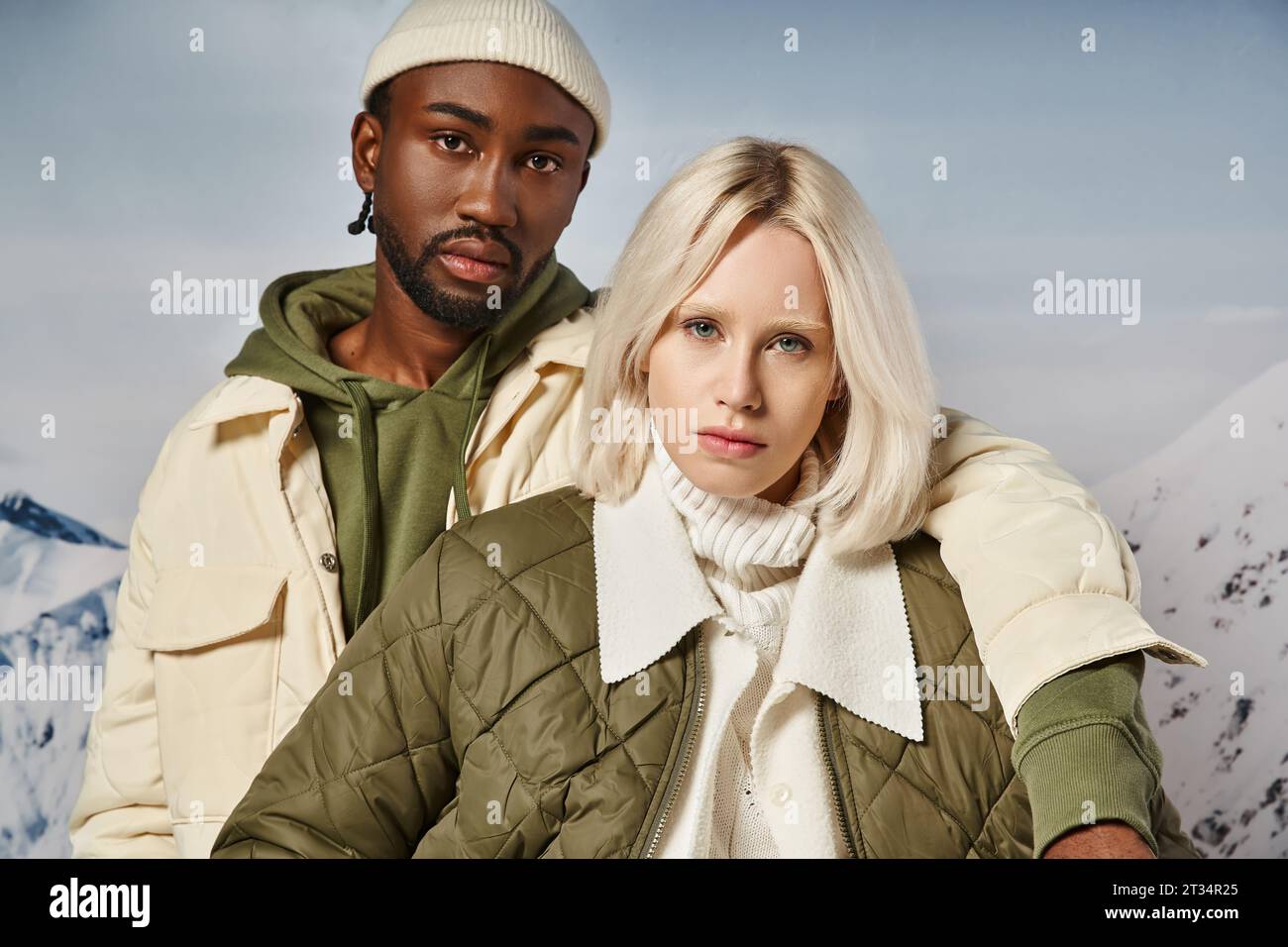 portrait of voguish multiracial couple in warm vibrant attire looking at camera, winter concept Stock Photo