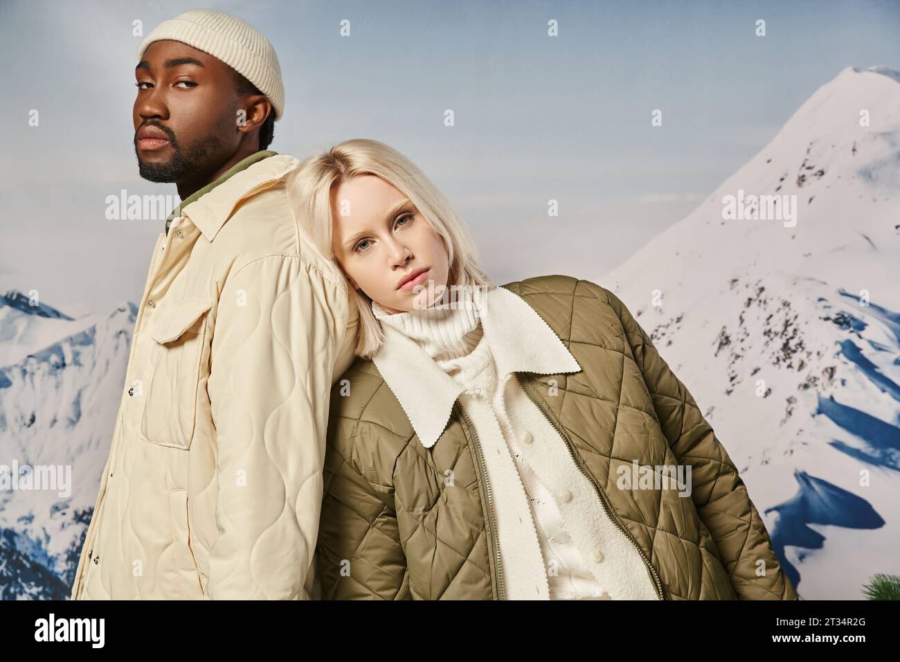 young interracial couple in warm clothes with mountain background looking at camera, winter concept Stock Photo