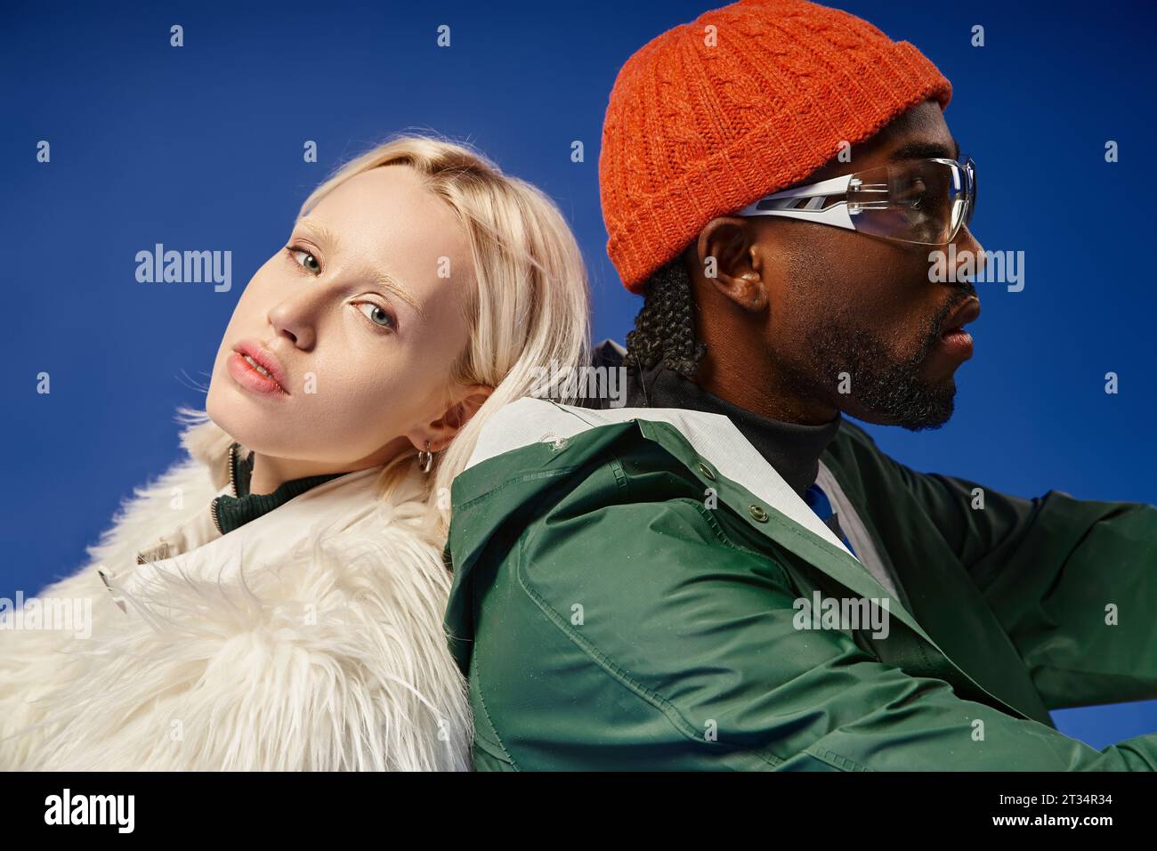 multicultural models in trendy winter outfits posing together on blue backdrop, diversity and style Stock Photo