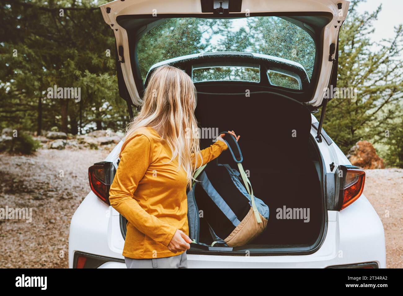 Woman puts backpack in a car trunk road trop vacations travel active lifestyle outdoor rental auto Stock Photo