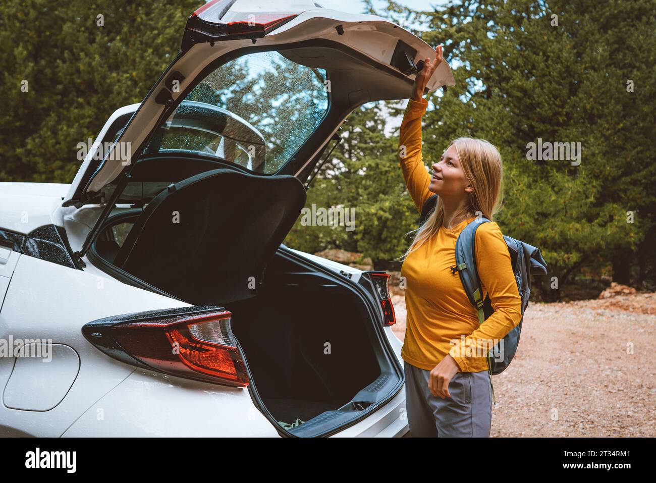 Woman driver traveling by car. Girl opens trunk. Road trip with rental auto summer vacations transport insurance concept Stock Photo