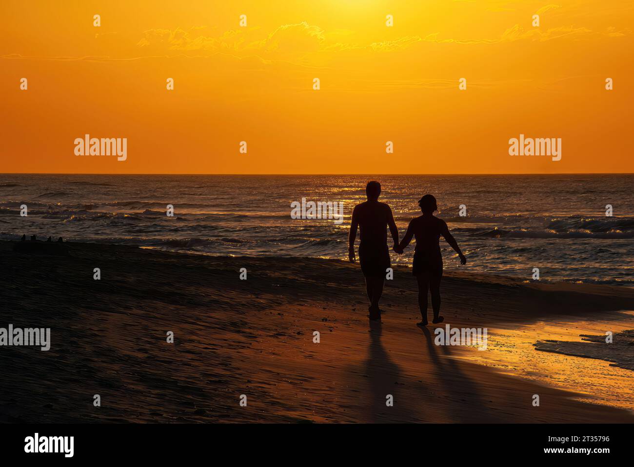 Silhouette of couple holding hands while walking on beach in a sunset ...
