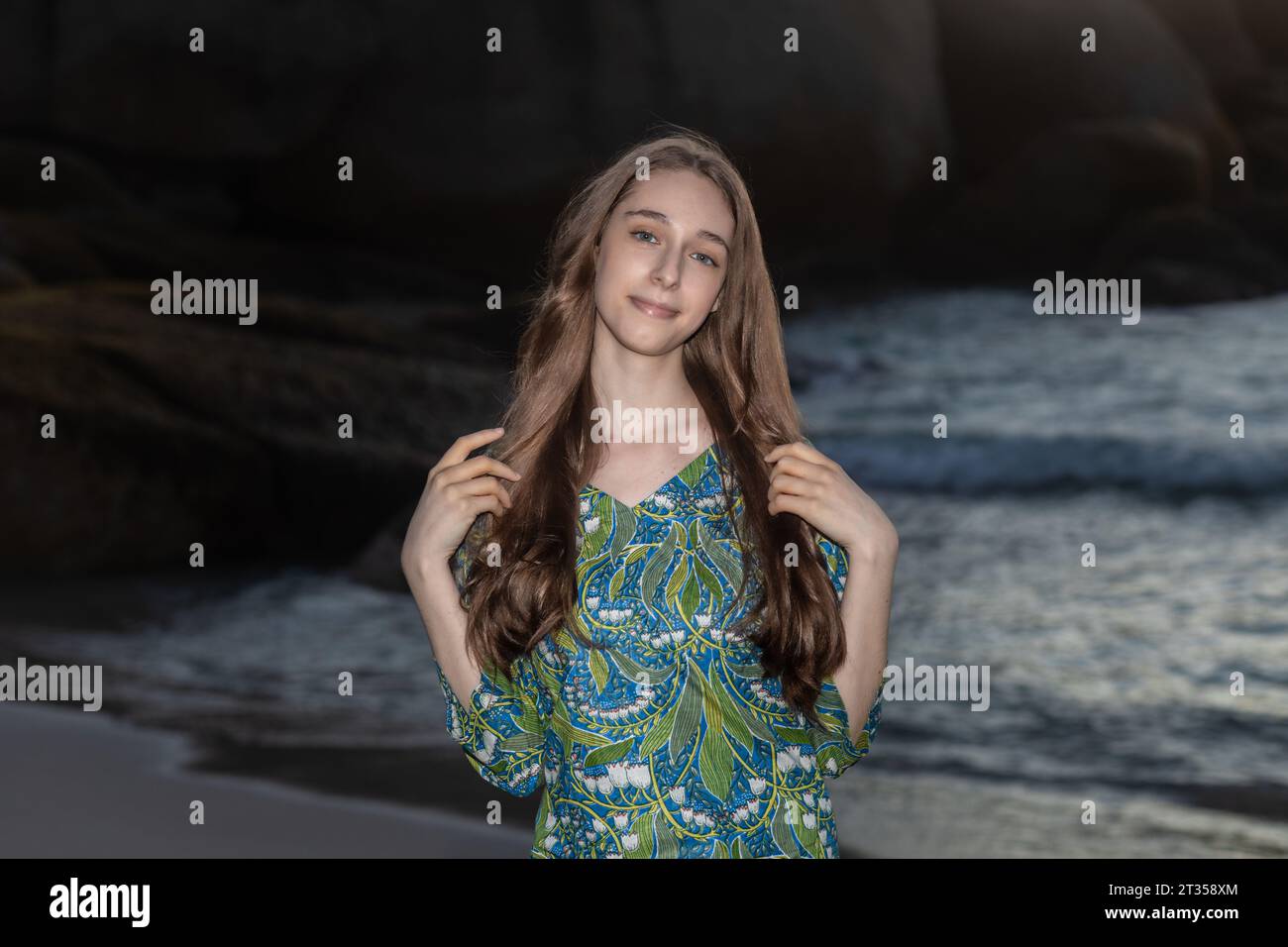 An elegant 20-year-old Caucasian woman with long flowing hair exudes grace in a close-up shot, donned in a green patterned shirt dress on the beach Stock Photo