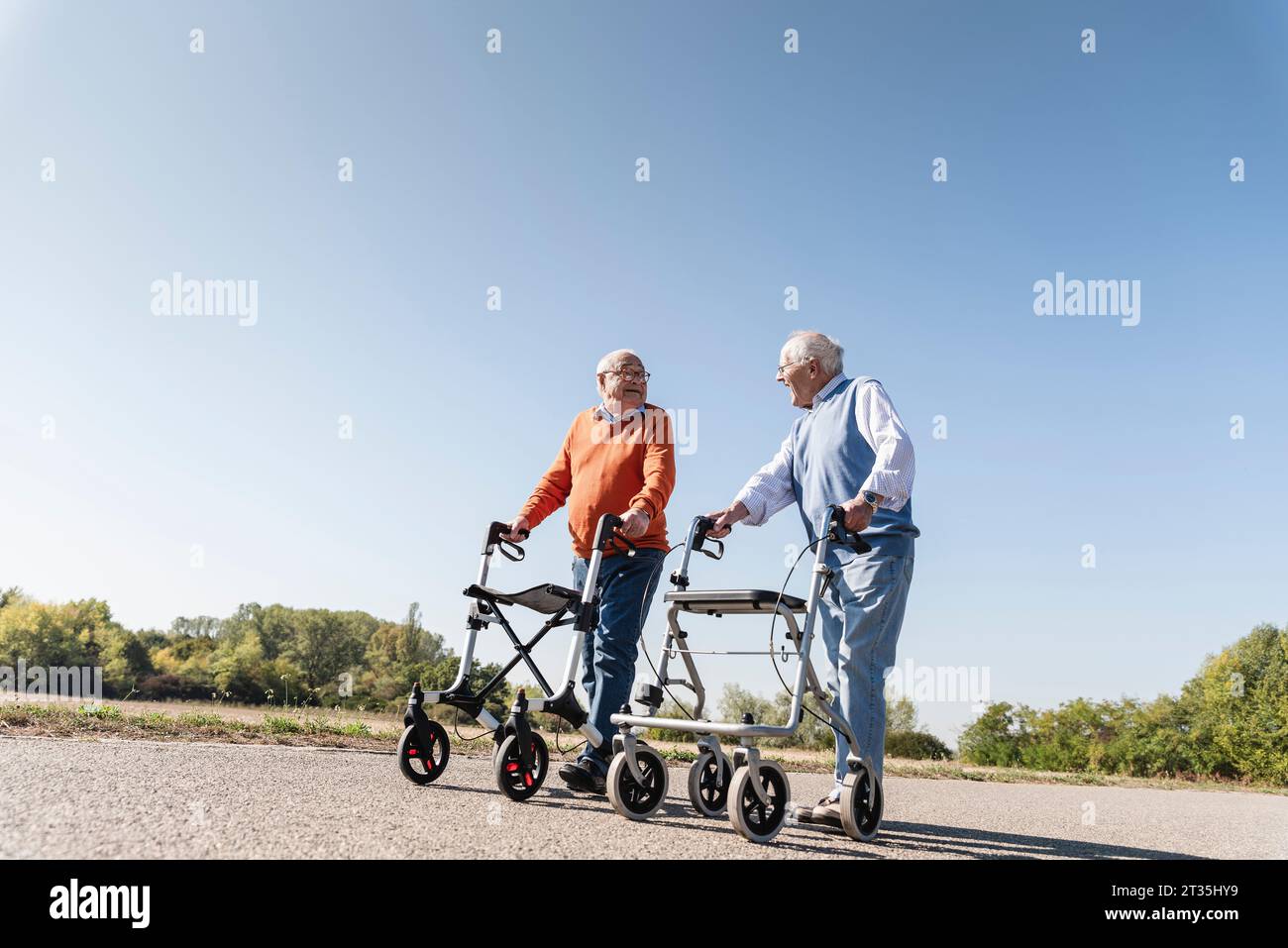 Two old friends walking on a country road, using wheeled walkers Stock