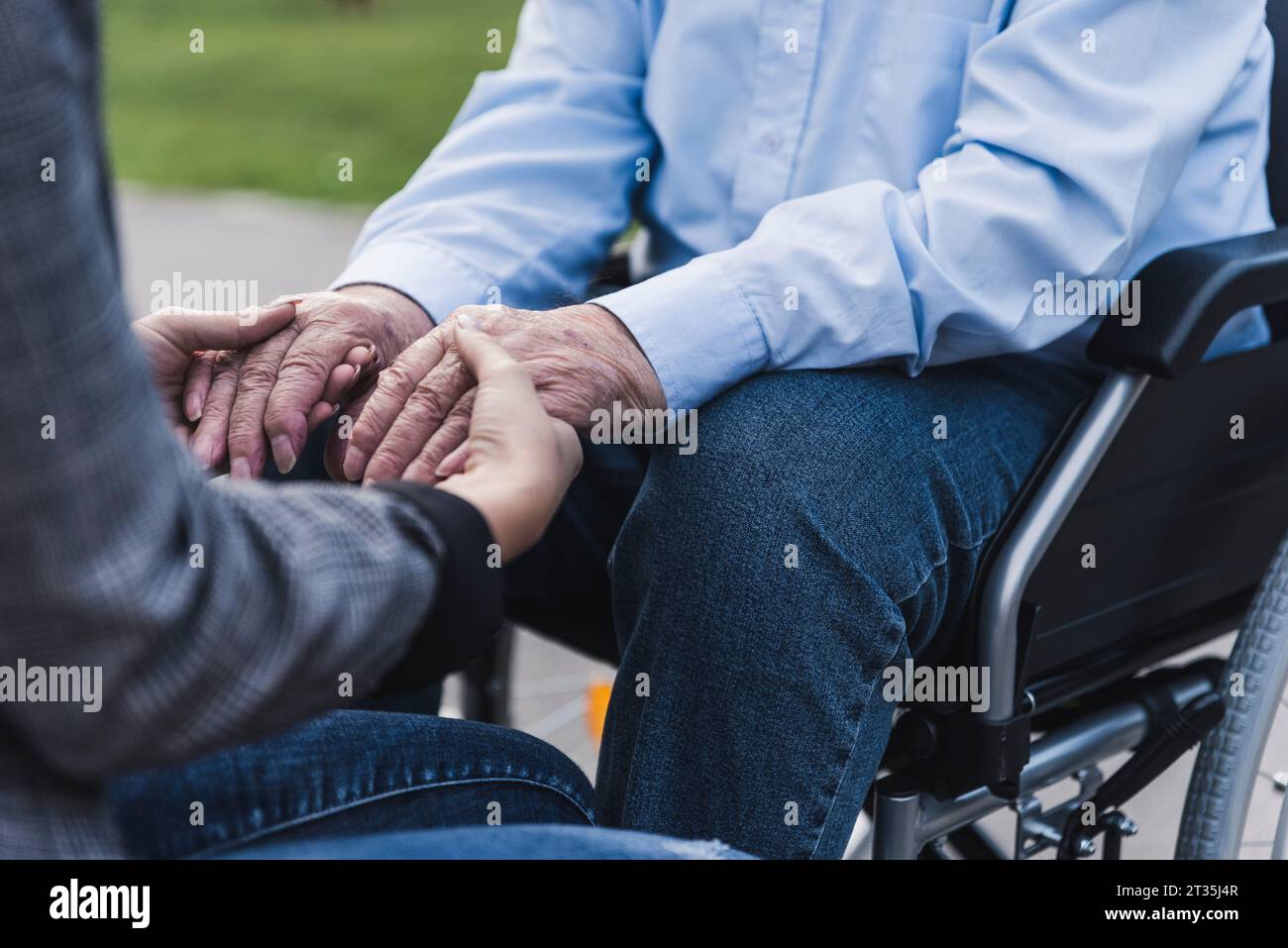 Young woman holding hands of senior man sitting in wheel chair, partial view Stock Photo